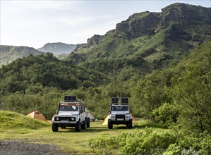 Two white Land Rover off-road vehicles on a campsite with tents