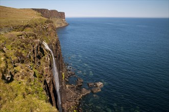 View of the coastline with a waterfall cascading over cliffs into the sea with Kilt Rock in the background