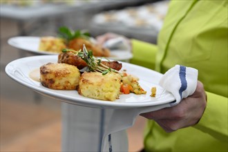 Service staff with plate of corn poulard breast with potato gratin and root vegetables