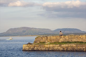 Man rod fishing on summers evening as boat heads out to sea. Sligo