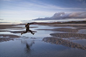 Man jumping over tidal sea puddles