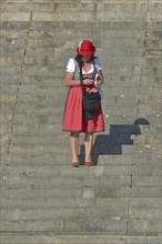Woman in red dirndl stands on stairs and looks into mobile phone