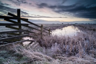 Cattle fence leading into ditch on frost-covered pasture at dawn