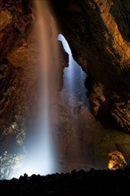 View of upland stream waterfall flowing down chasm into chamber of cave