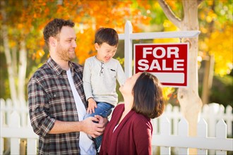 Young mixed-race chinese and caucasian family in front of for sale real estate sign and fall yard