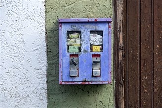 Old chewing gum machine filled with chewing gum and children's toys on the wall of a house