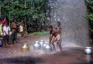 Silvery shower. Boys playing the water spray from the leakage of drinking water pipe line near Coimbatore