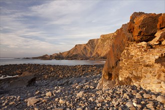 Man-made dyke and coastal cliff with folded layers at sunset