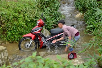 Boy washes motorbike in stream