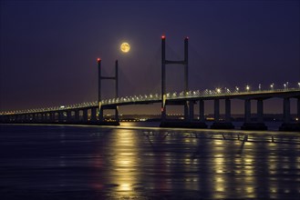 View of road bridge over river at dusk under full moon
