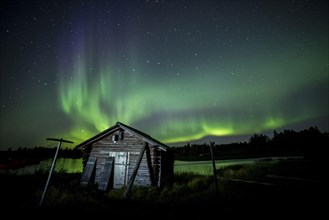 Aurora Borealis and stars over fishing hut and lake at night