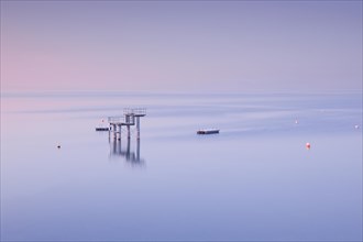 Rosa-violette Abendstimmung ueber dem Bodensee mit Blick zum Sprungturm und den Flossen der Freibadanlage Horn inmitten des Sees