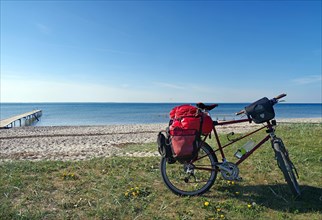 Bicycle with luggage in front of a lonely sandy beach with jetty