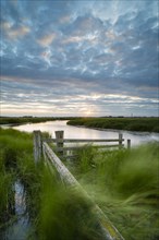 Cattle fence and flooded ditch in coastal grazing marsh in strong wind at sunset