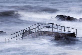 Tidal pool steps above breaking waves during incoming tide on windy morning