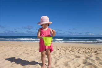 Toddler girl holding a green bucket at the beach