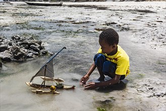 Kind spielt im flachen Wasser mit selbst gebautem Boot