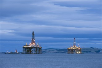 Oil rigs moored in sea near coast at dusk