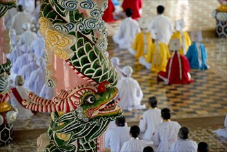 Caodaist disciples sitting beside colourful columns with dragons during ceremony