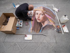 Strassenkuenstler malt ein Bild mit Kreide auf den Asphalt
