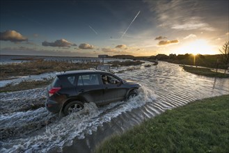 4x4 driving through flooded coastal road along post-flood coastal marsh