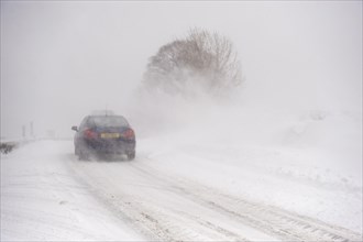 Car driving on a country road during a heavy snowstorm