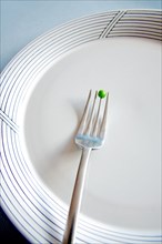 Afork with a single pea on an empty plate