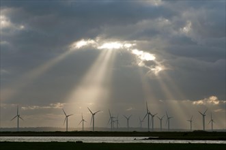 Wind turbines on windfarm with sunbeams through clouds at sunset