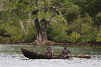 Two boys paddling a dugout canoe