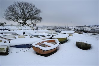 Snow covered boats moored at the edge of the mudflats