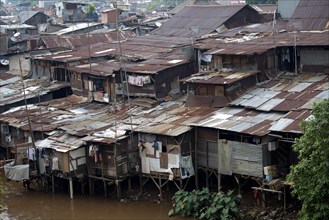 Stilted shacks with corrugated iron roofs beside river in city