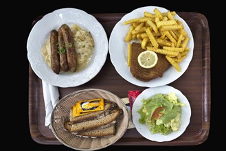 Bratwurst with sauerkraut and bread and cordon bleu with french fries on a tray on a black background