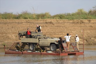 Safari vehicle and tourists crossing the river on a pontoon