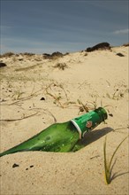 Glass beer bottle discarded on sandy beach