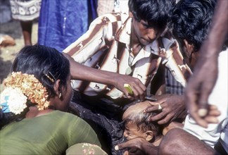 Indian Hindu devotees tonsuring or shaveing their baby head as an offering during Chitra or Chithirai festival in Madurai Tamil Nadu