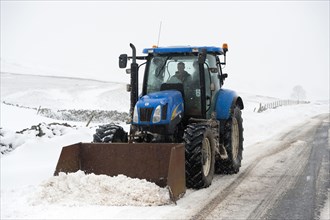 New Holland tractor clears snow from country road after snowstorm