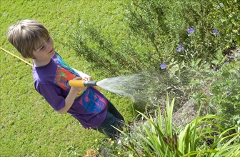 Boy watering plants in garden with hose