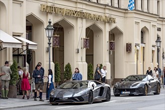 Parked Lamborghini Aventador and Ferrari F12 Berlinetta sports cars in front of Hotel Vier Jahreszeiten Kempinski