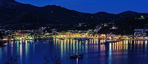 Panoramic view of Porto Azzurro with illuminated harbour promenade in the evening mood during blue hour