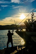 Backlight shot of silhouette of angler casting fishing rod in harbour just in front of sunset