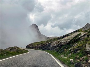 Dense cloud Wall of clouds pushes over high narrow mountain road above tree line