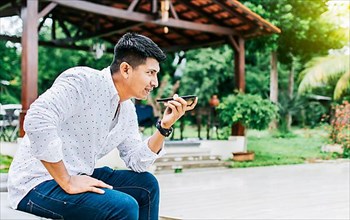 Handsome man sitting outside sending a voice message with his cell phone