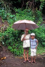 Two boys standing with an umbrella and one boy crying fearing for camera in Attappadi