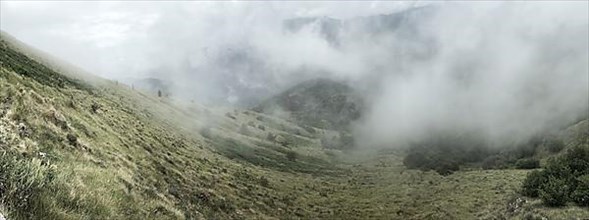 Panoramic view of low-hanging clouds in valley of mountain landscape in Alps