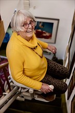 Senior woman laughing at home riding the stair lift up the stairs