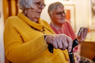 Senior citizen with crutch is shown a smartphone by her sister
