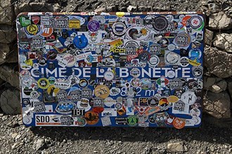 Sticker-covered official sign indicating altitude of 2802 metres above sea level from Cime de la Bonette