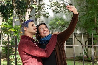 Two friends are taking selfies outdoors. He has blue hair