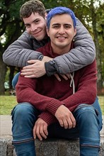 Gay male couple hugging and looking at camera outdoors