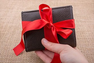 Hand holding a gift wallet wrapped with red ribbon